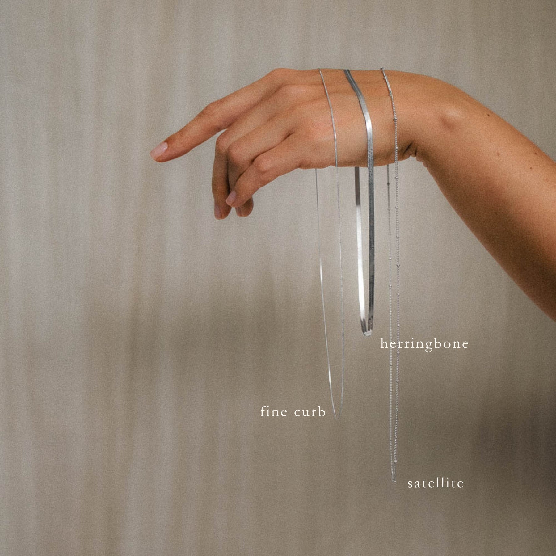 hand holding three labelled hanging necklace chains herringbone, satellite and curb