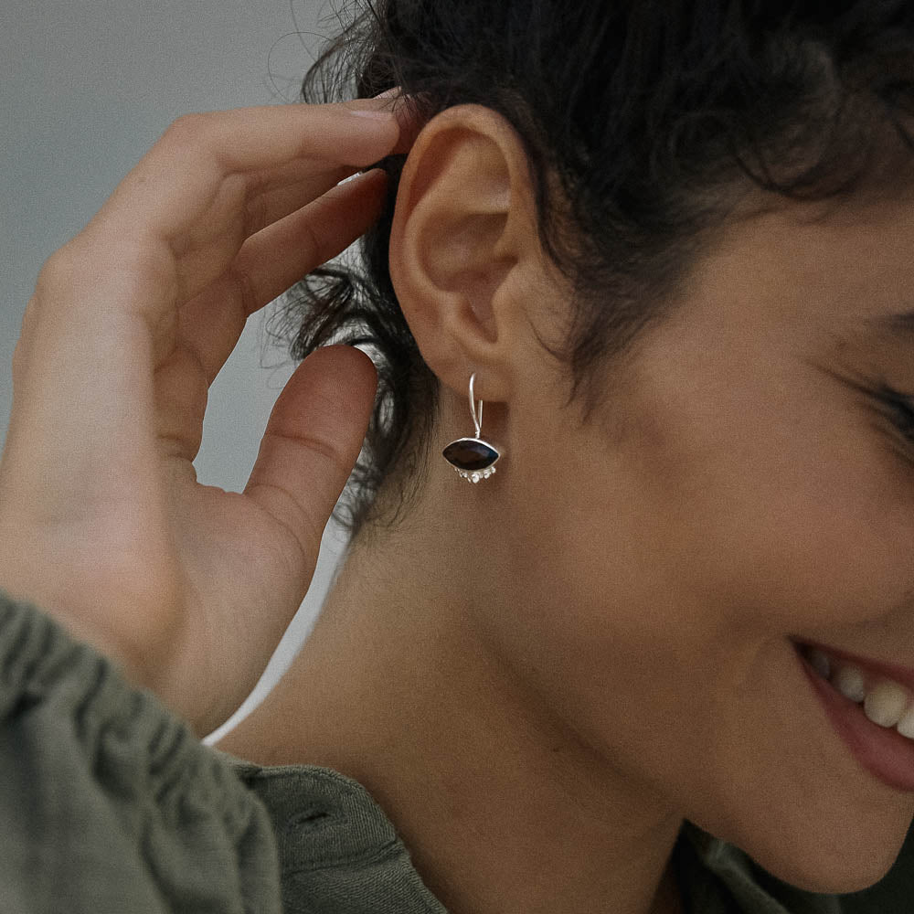 Close-up of a person wearing an natural Smokey Quartz earring with a dark stone and clear gem, smiling.