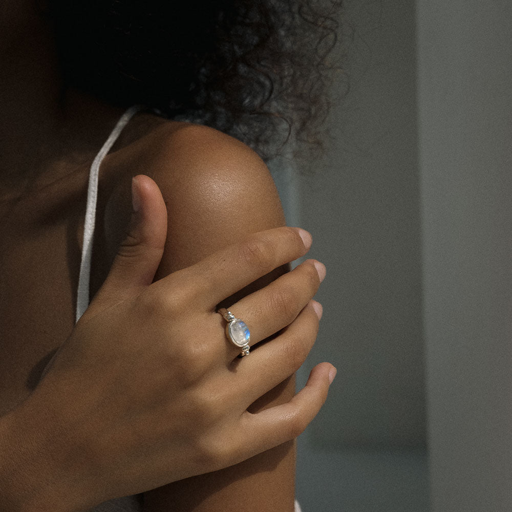 Woman wearing a silver ring with a blue moonstone geme on a neutral background