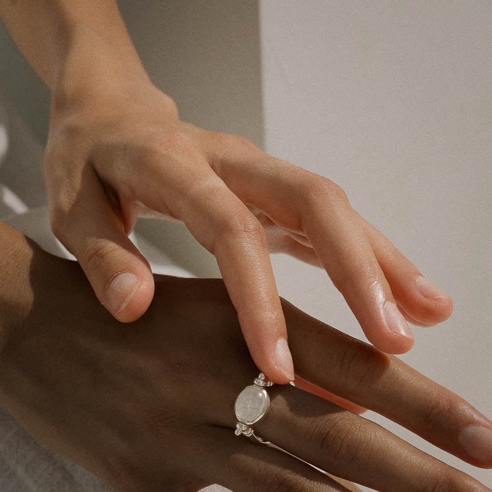 Close-up of a hand wearing a ring with a light-colored stone on a neutral background
