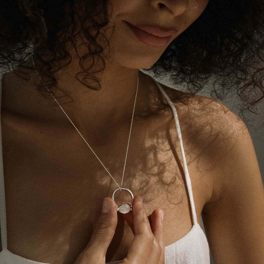 Woman wearing a silver necklace with a circular pendant, close-up shot.