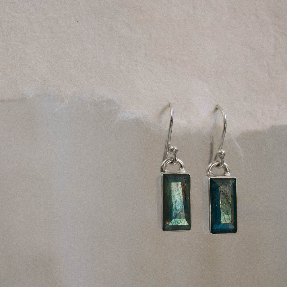 a pair of baguette labradorite silver earrings hanging on a piece of handmade paper