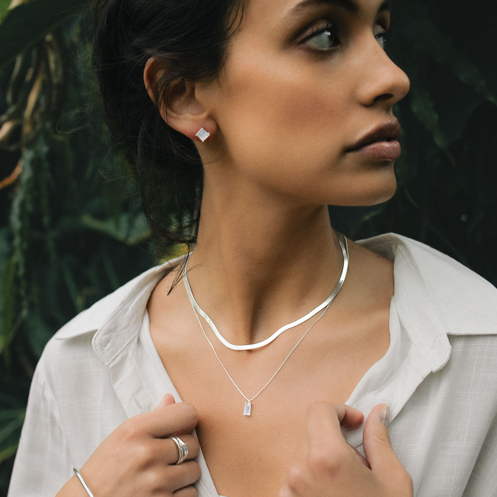 a woman wearing silver baguette vertical moonstone necklace in a jungle with a white shirt on looking to the side