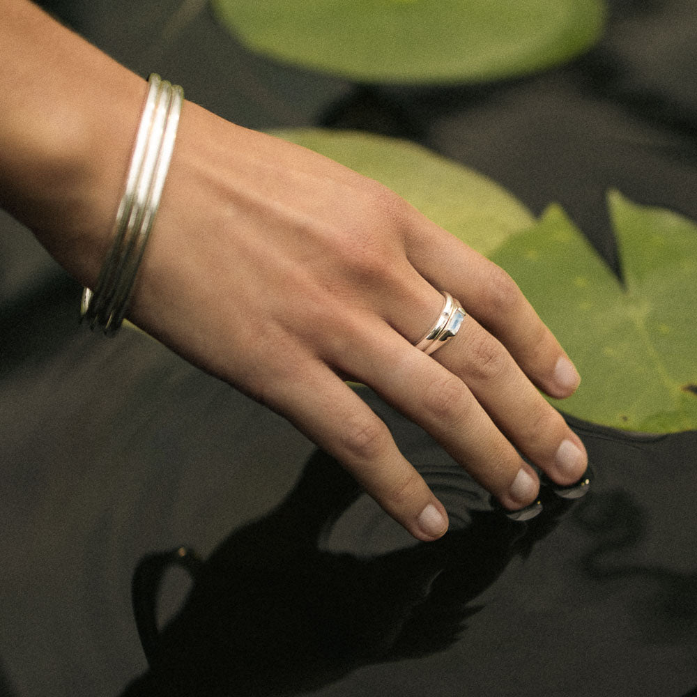 a woman wearing silver bangles and a moonstone baguette ring by a beautiful waterlily pond