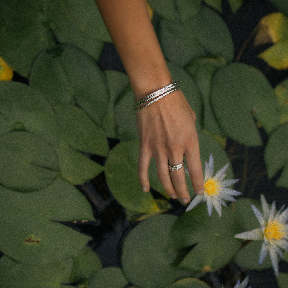 a woman's hand touching a water lily wearing three sterling silver bangles and rings