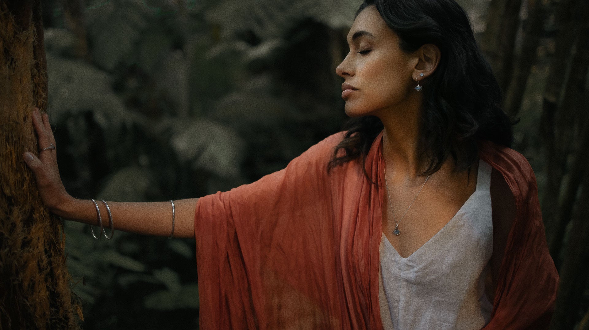 a bohemian woman wearing silver jewellery grounding herself with hand against a tree