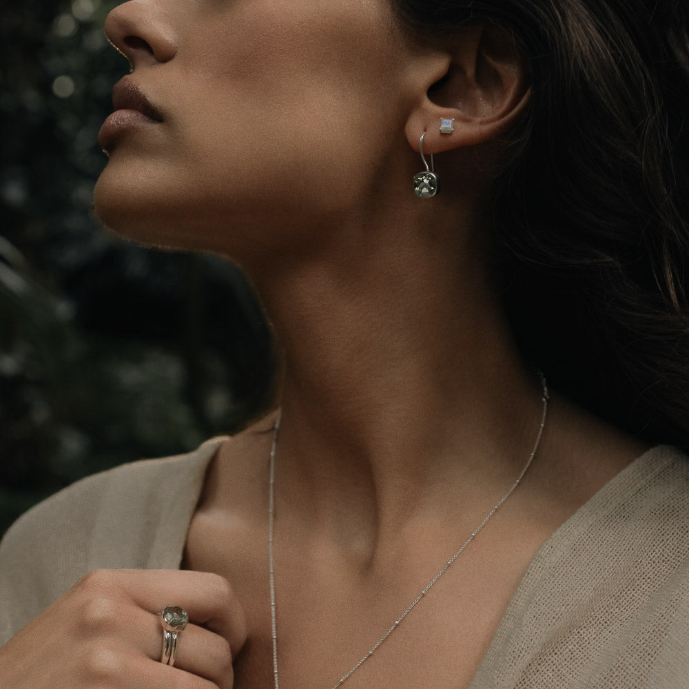 a woman wearing a pair of green amethyst square faceted earrings  and ring