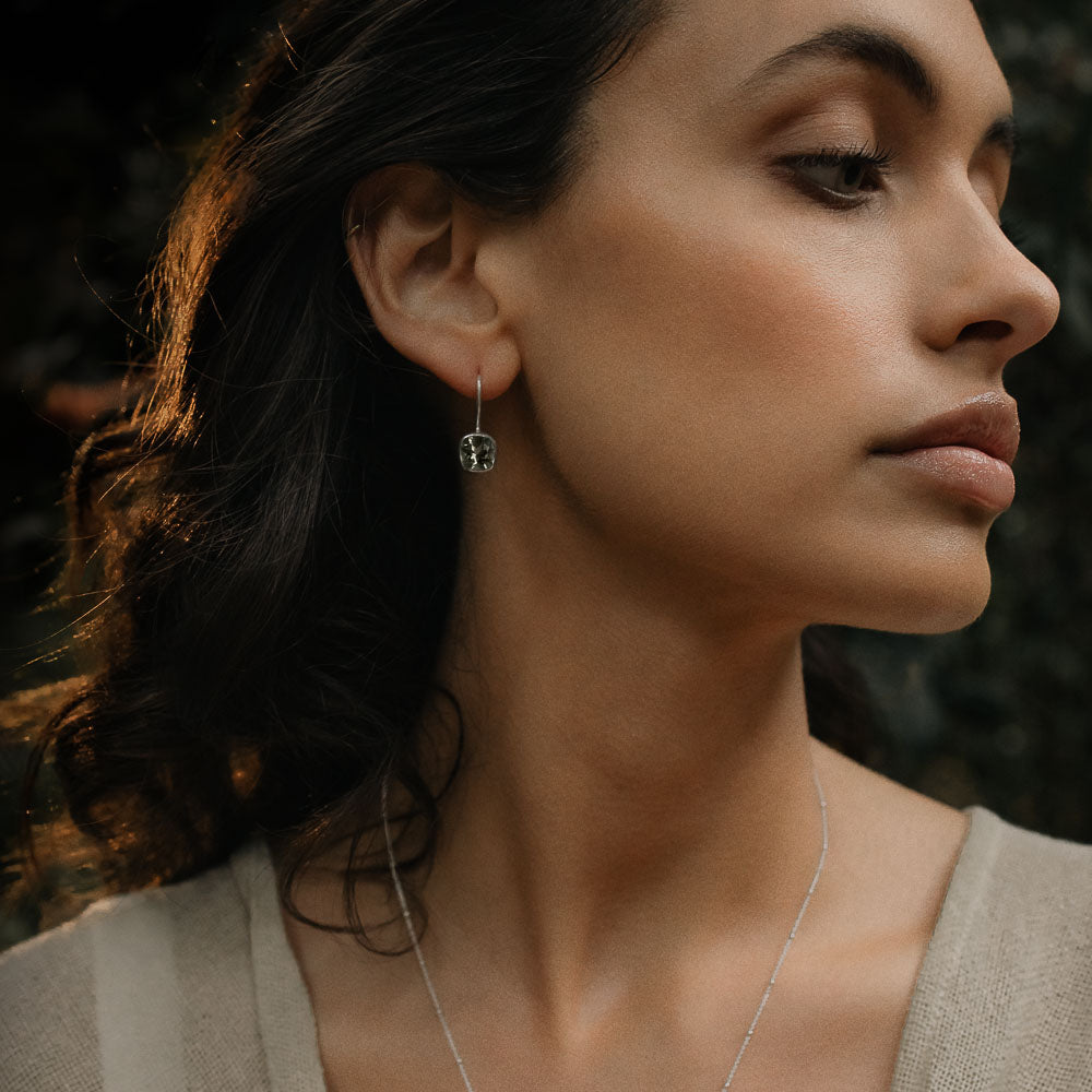 a woman wearing a pair of green amethyst square faceted earrings a woman's middle finger touching a palm frond
