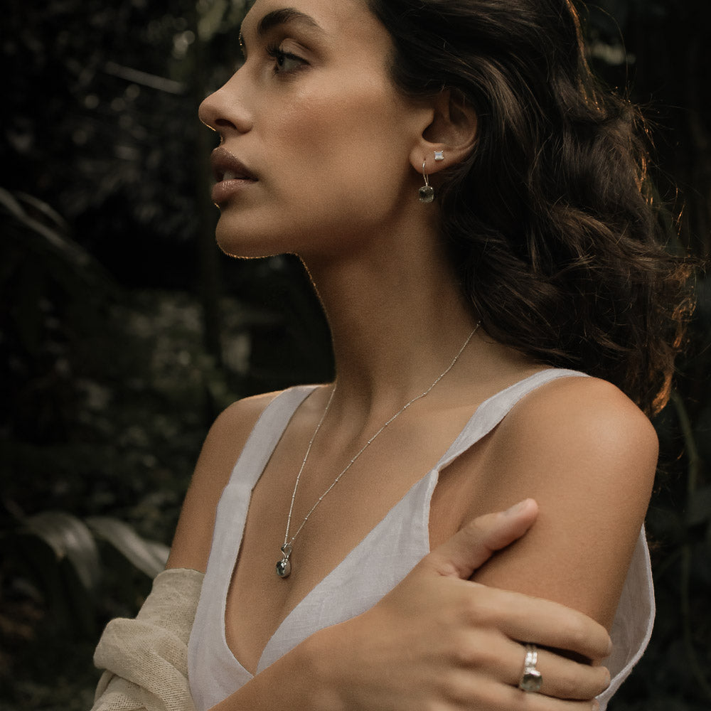 a woman wearing green amethyst gemstone pendant on silver chain in the lush forest