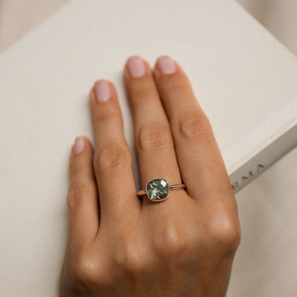 a woman wearing a green amethyst gemstone ring on her middle finger holding a book