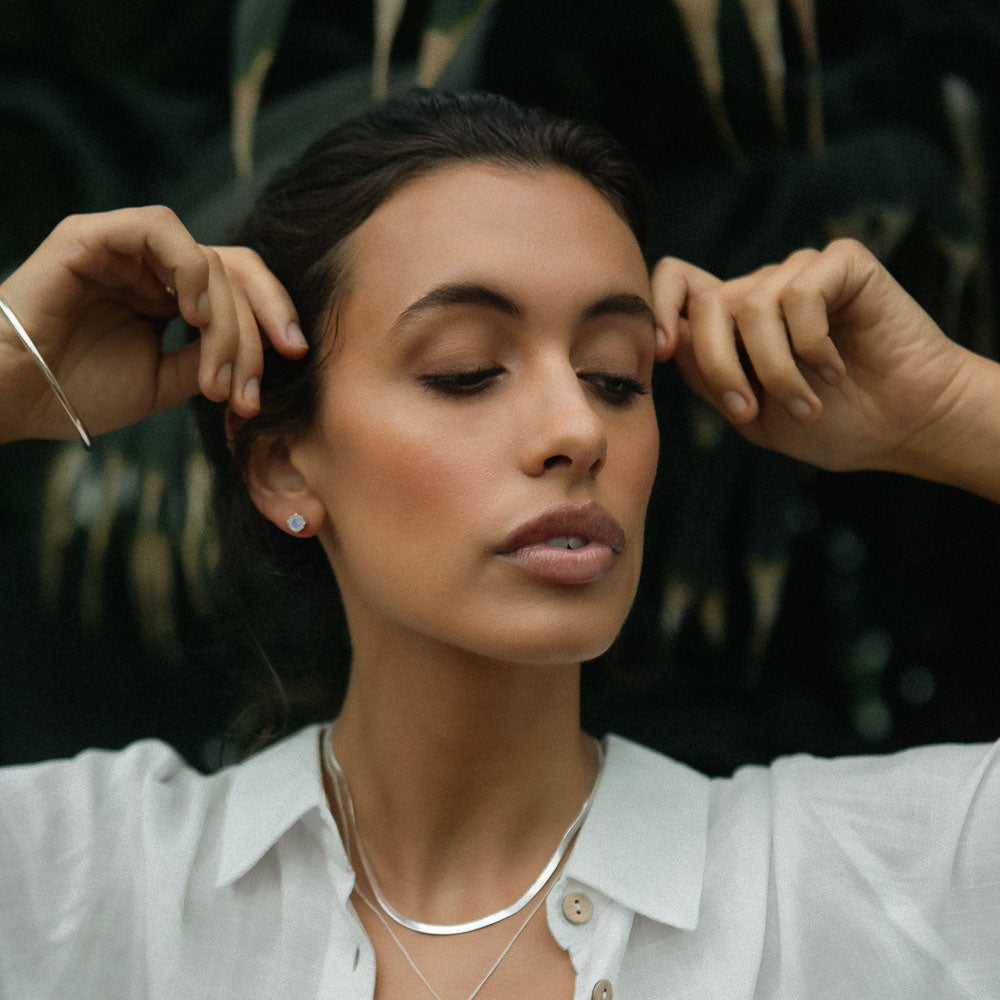 woman with arms up wearing round moonstone earring studs