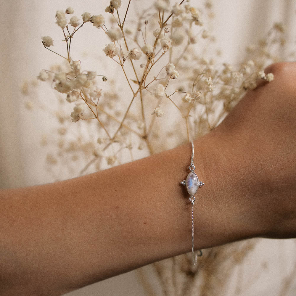 a womans arm wearing a marquise moonstone bracelet with tiny flowers behind
