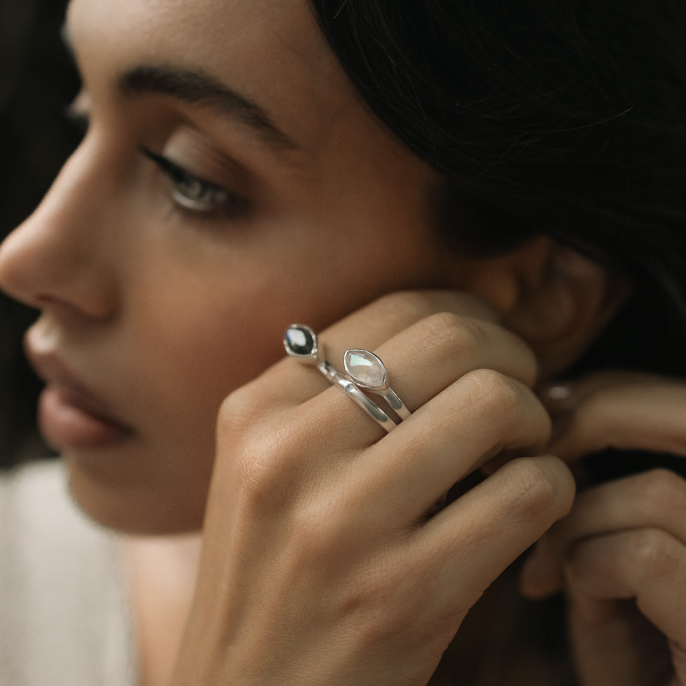woman wearing marquise moonstone and labradorite gemstone rings as she puts and earring in