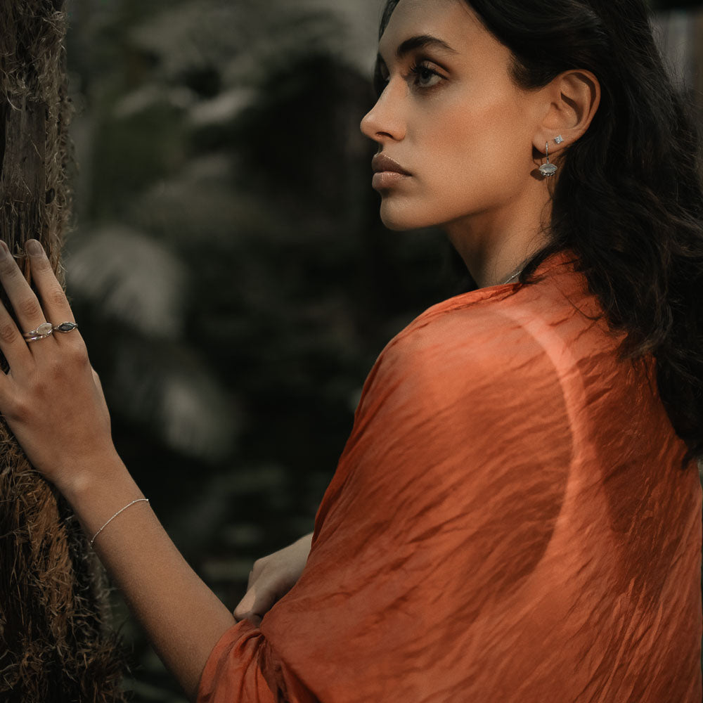 a woman with her hand on a tree wearing marquise moonstone gemstone earrings