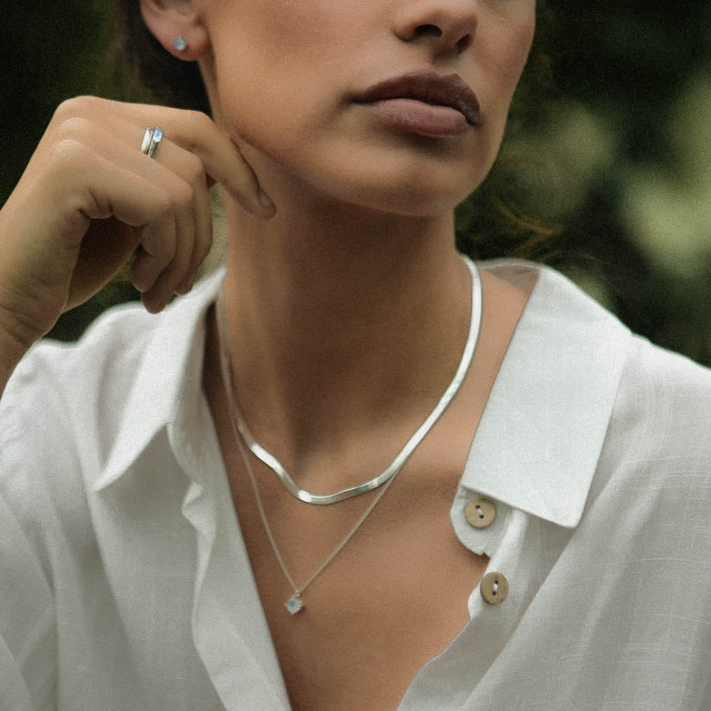 a woman wearing a moonstone baguette ring and silver necklace chains