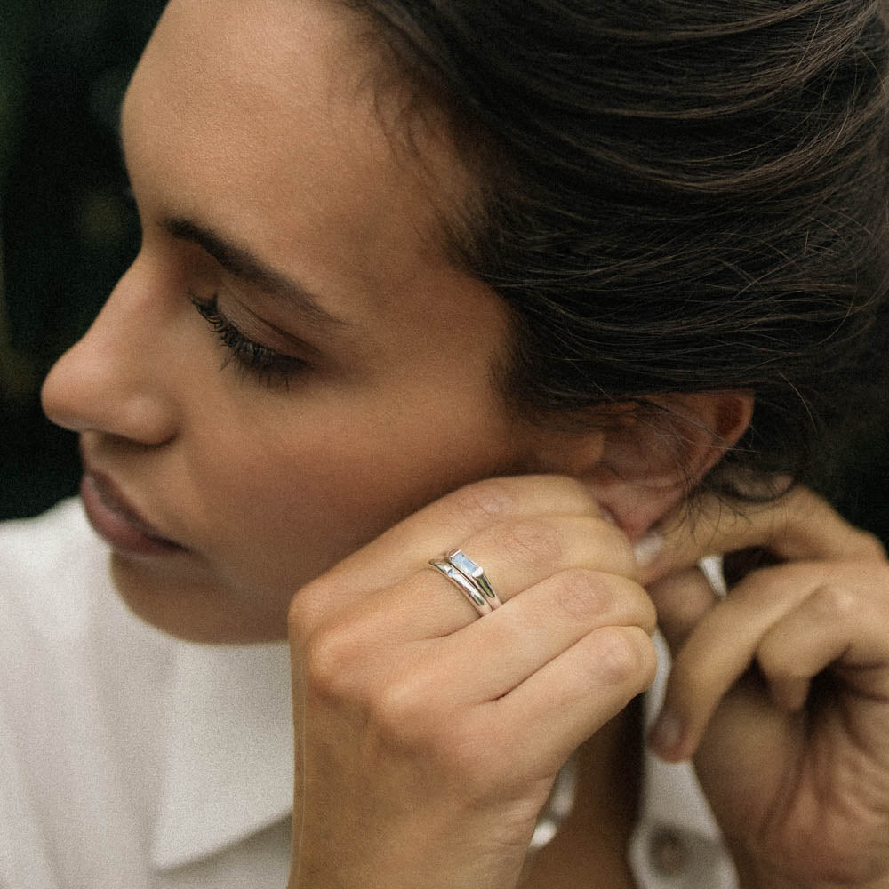 a woman wearing dainty round silver moonstone ring as she puts in an earring