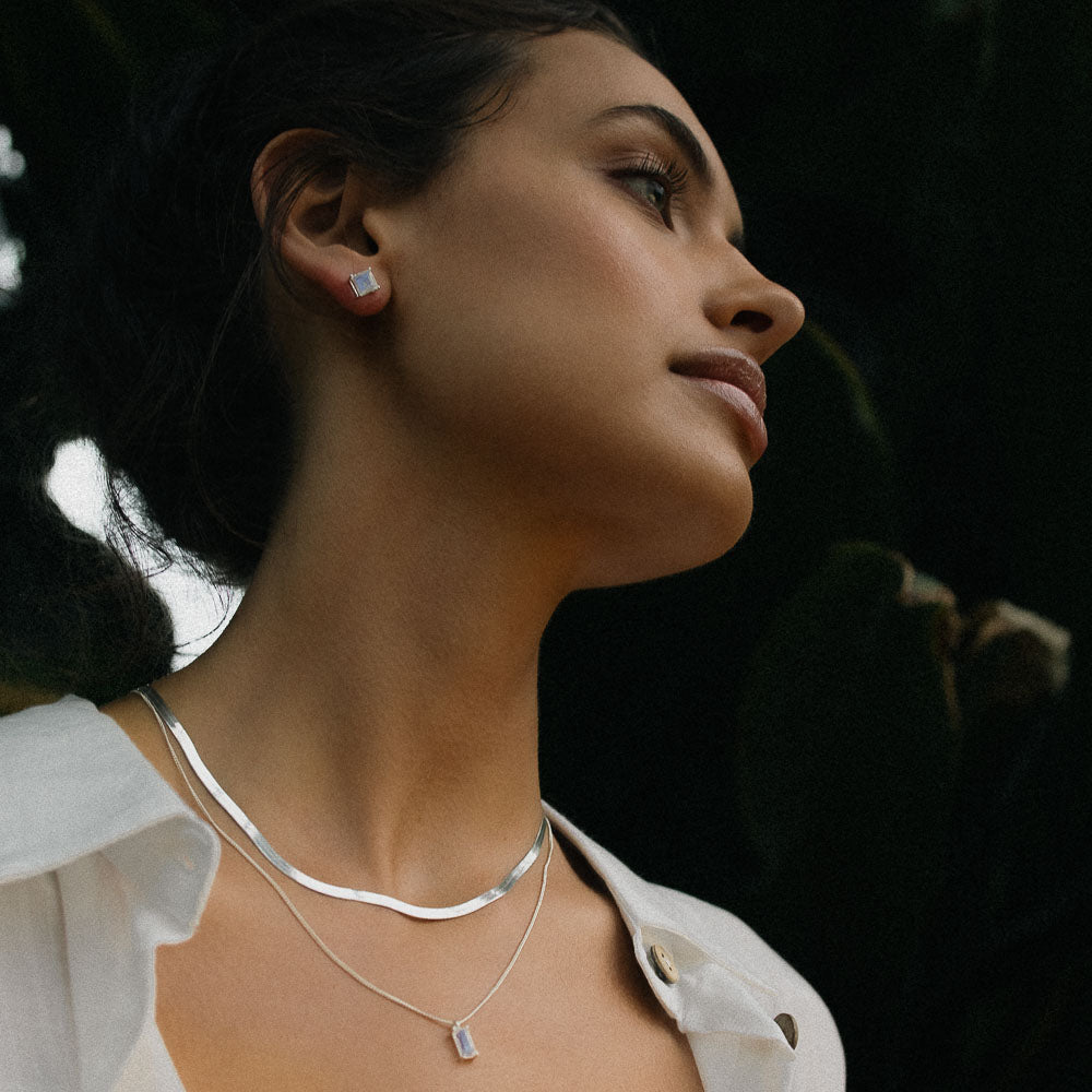 a woman wearing silver baguette vertical moonstone necklace in a jungle with a white shirt on