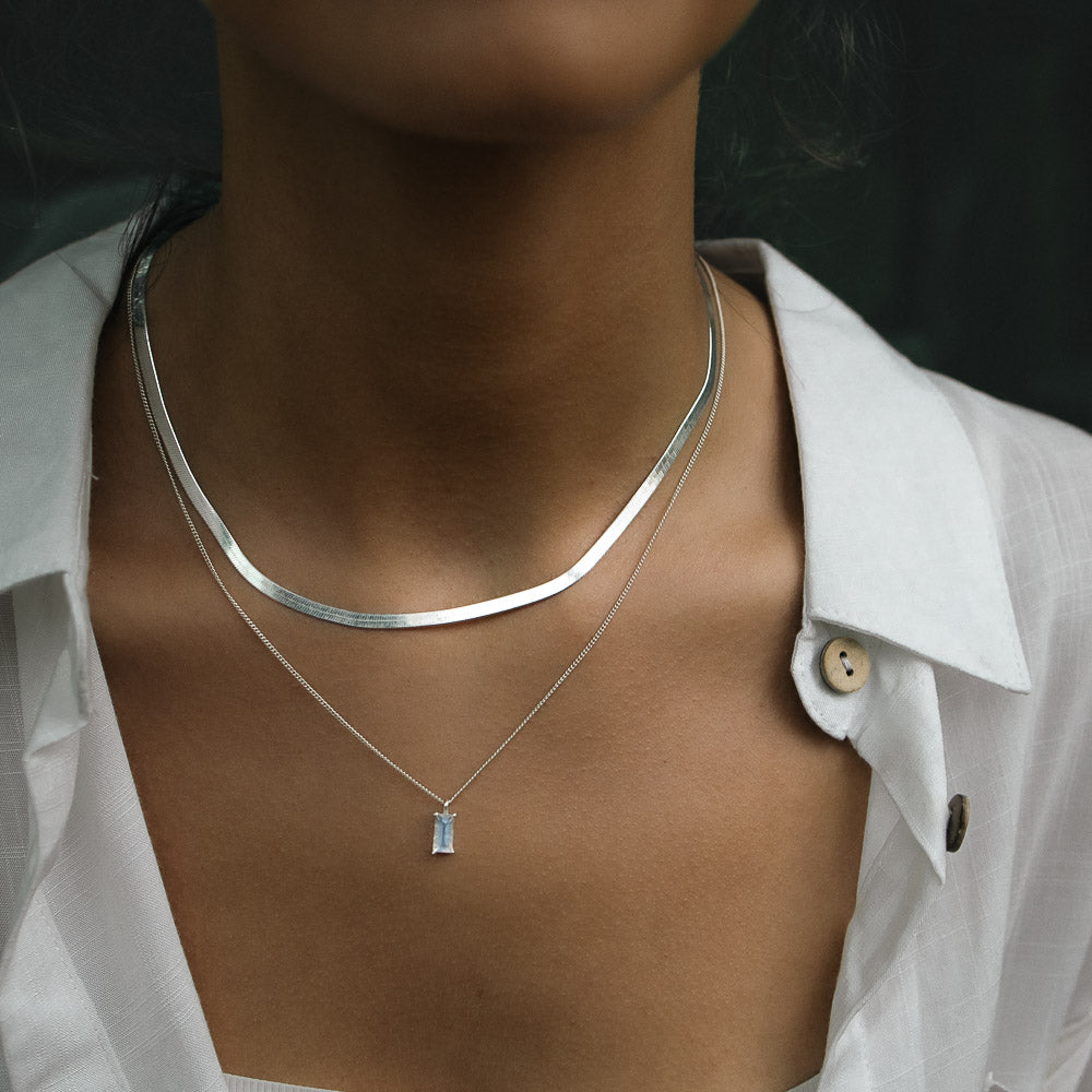 a woman wearing silver baguette vertical moonstone necklace in a jungle with a white shirt on