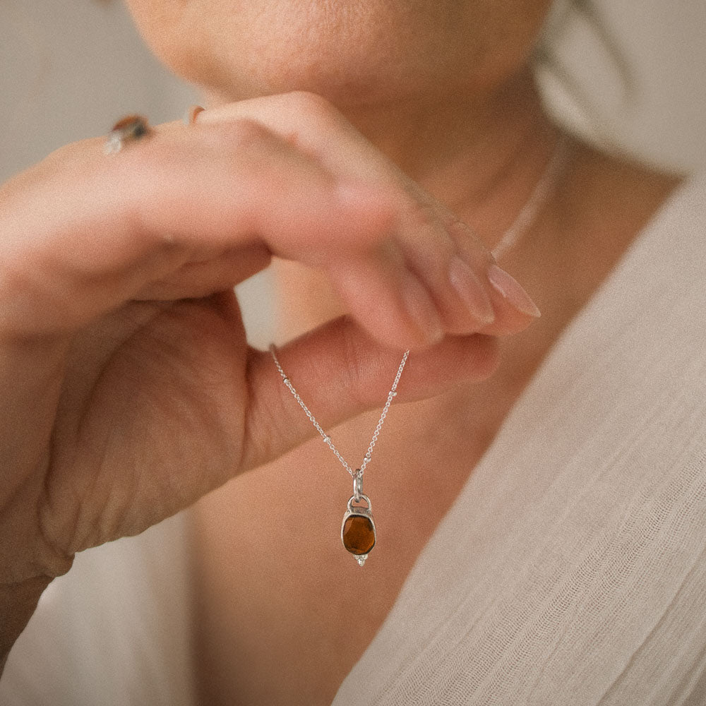 woman holding a orange tourmaline pendant on chain