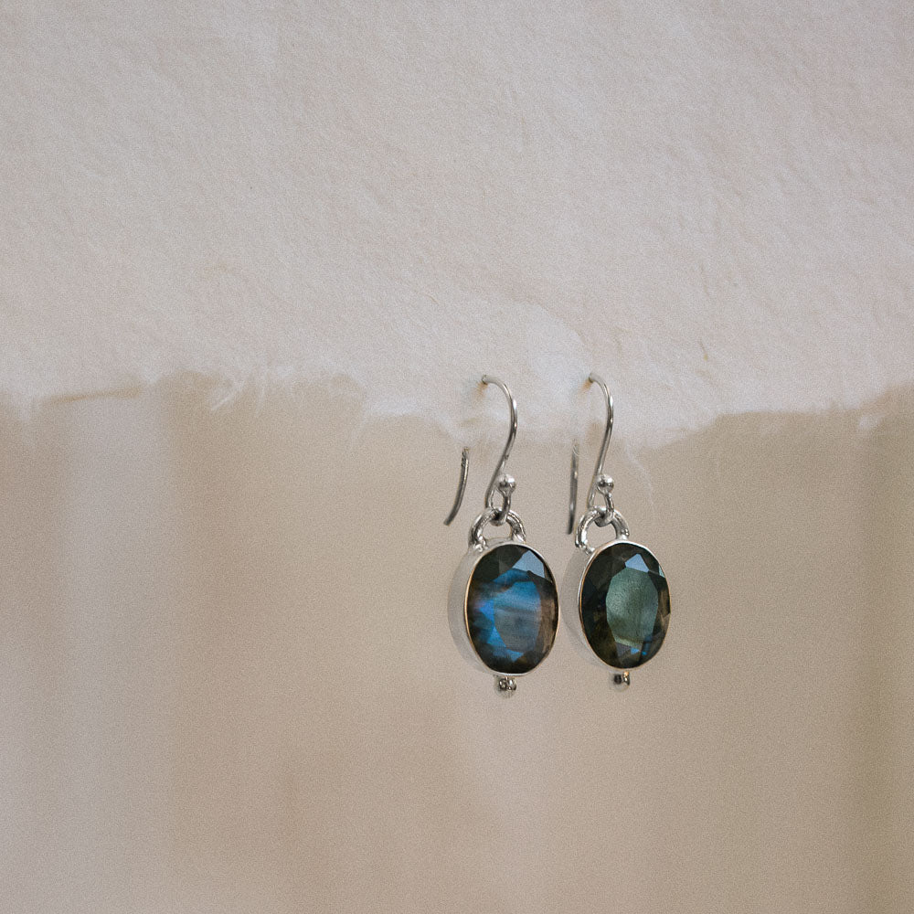 a pair of blue flashing oval labradorite earring hanging on paper
