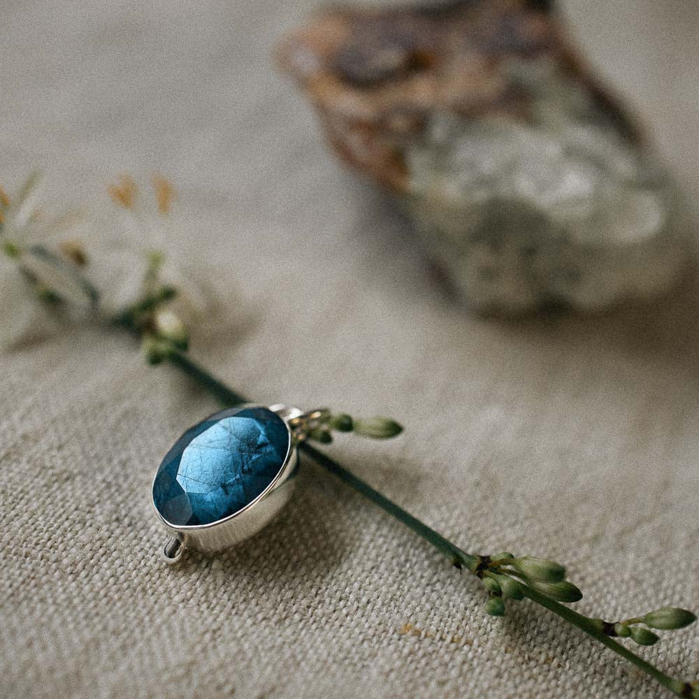 a blue flashing oval gemstone labradorite pendant on linen cloth with flower and crystal