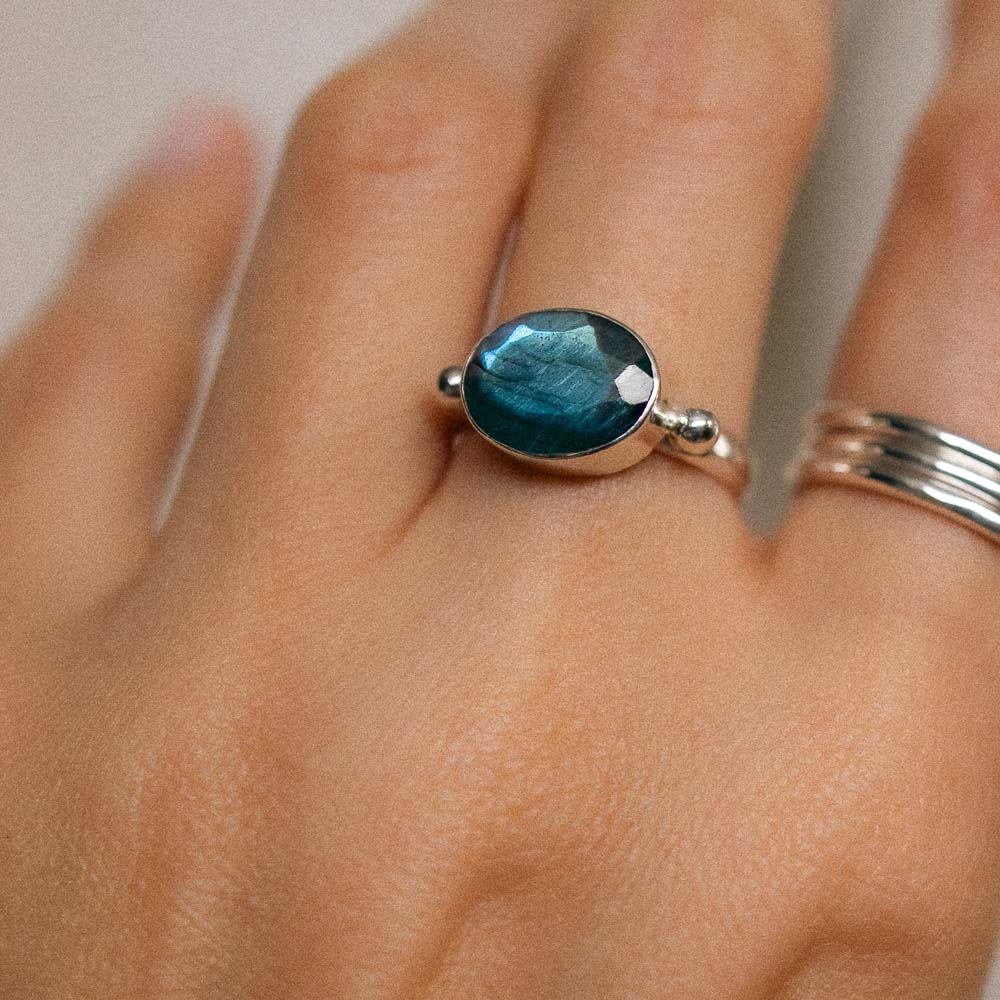 a silver oval gemstone labradorite ring on middle finger