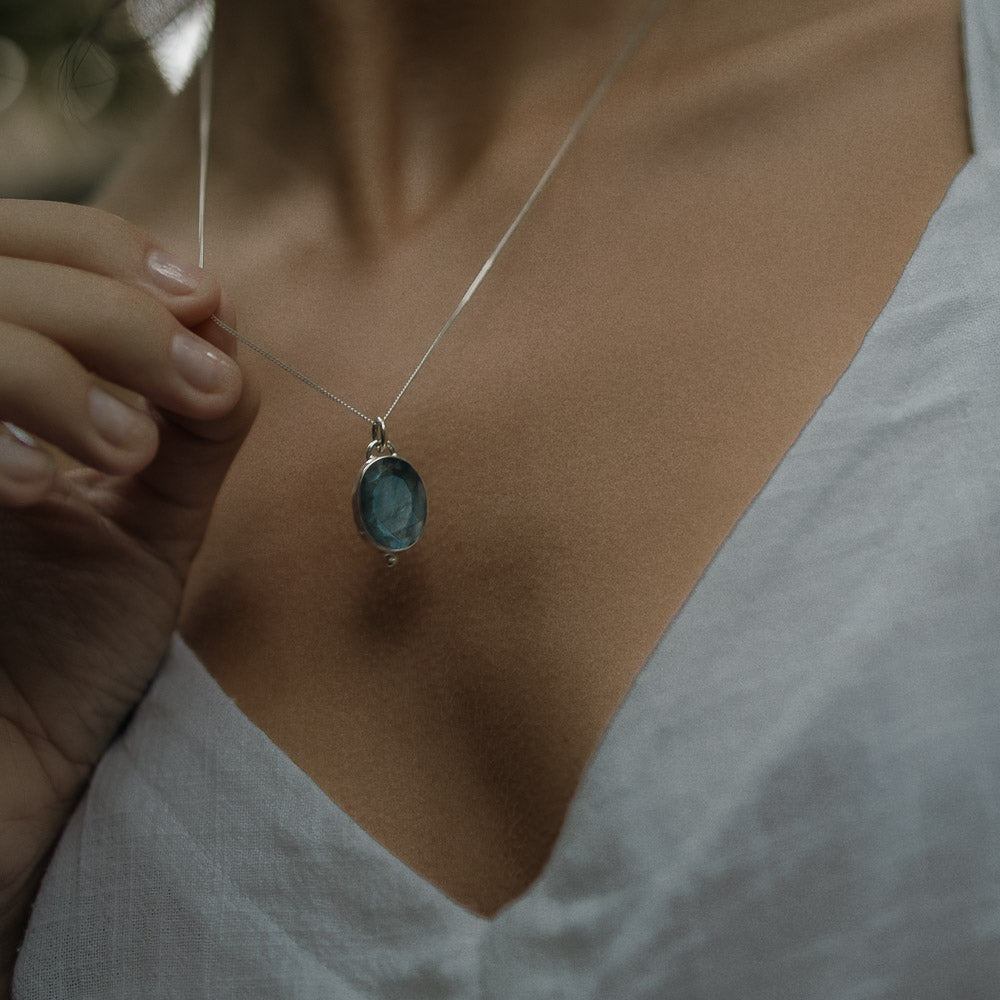 a blue flashing oval labradorite pendant hanging on a fine curb silver necklace chain on models neck