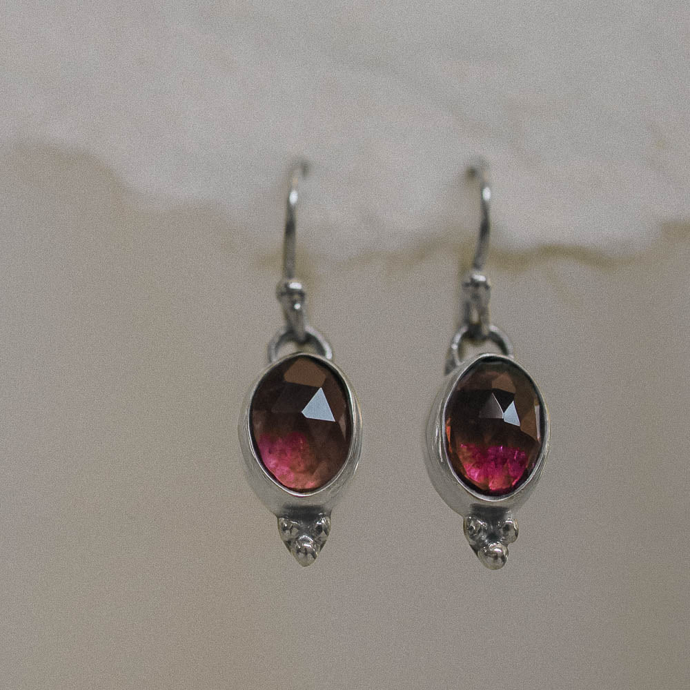 a pair of pink tourmaline earrings hanging on handmade paper