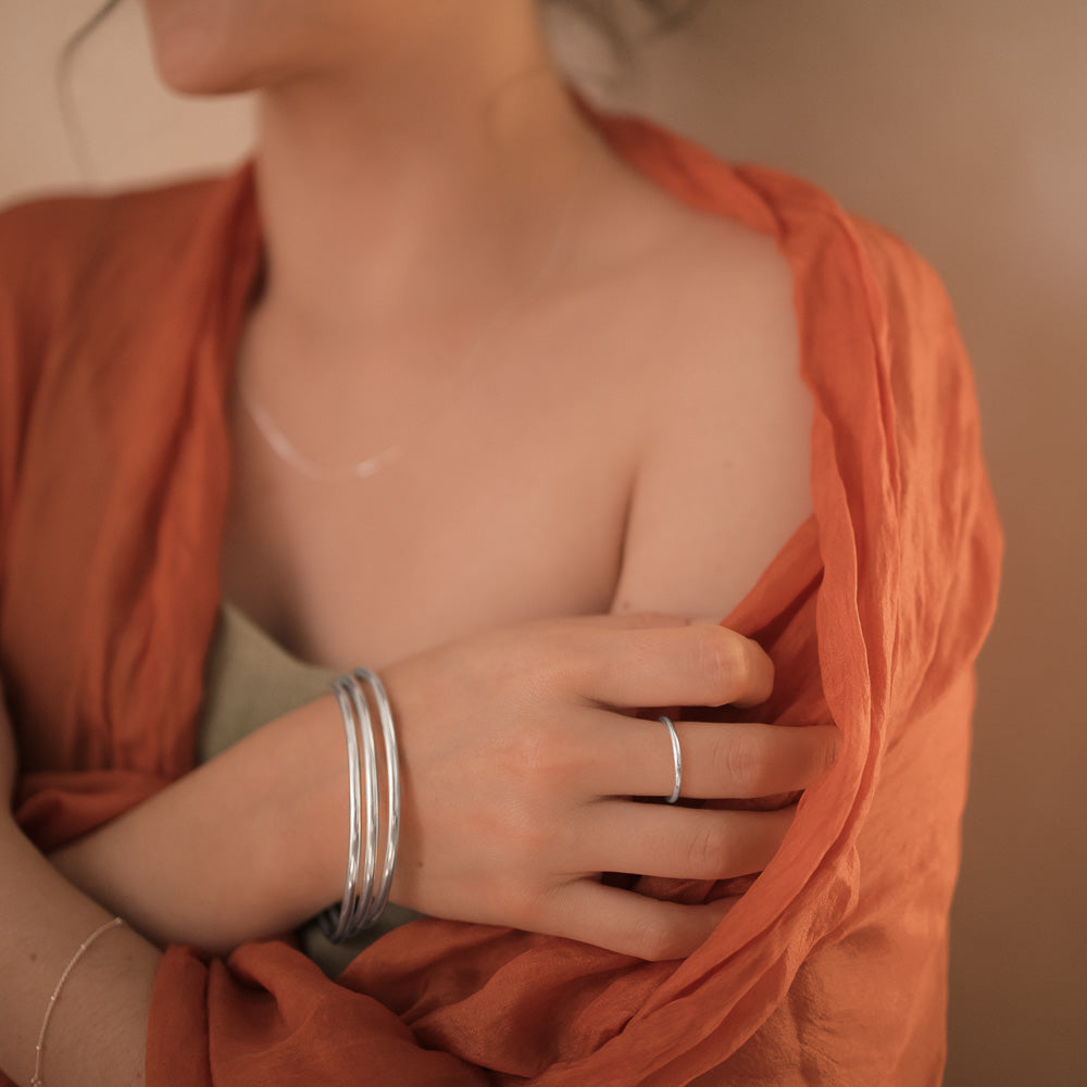 a woman wearing three sterling silver bangles and a silver band ring with rustic scarf over her shoulders