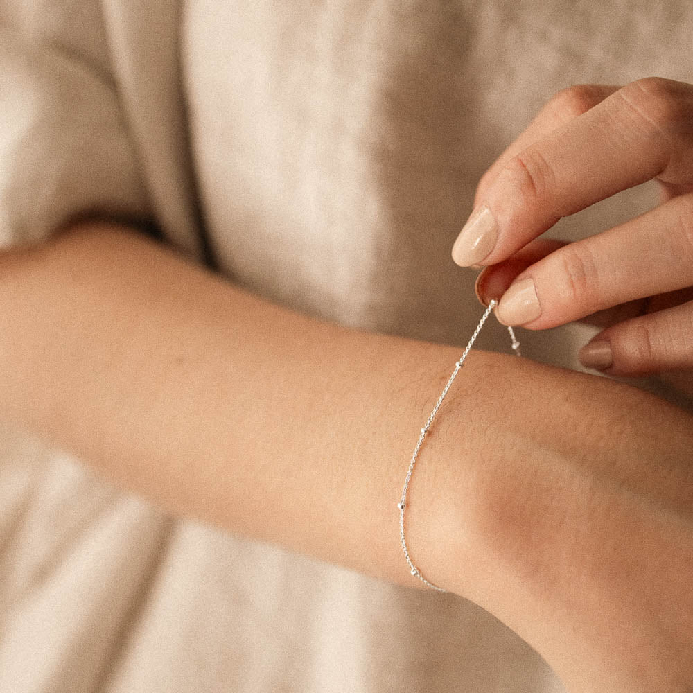 a woman touching a silver satellite bracelet chain on her wrist