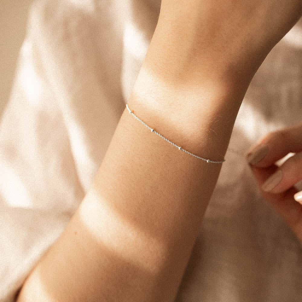 a woman touching a silver satellite bracelet chain on her wrist