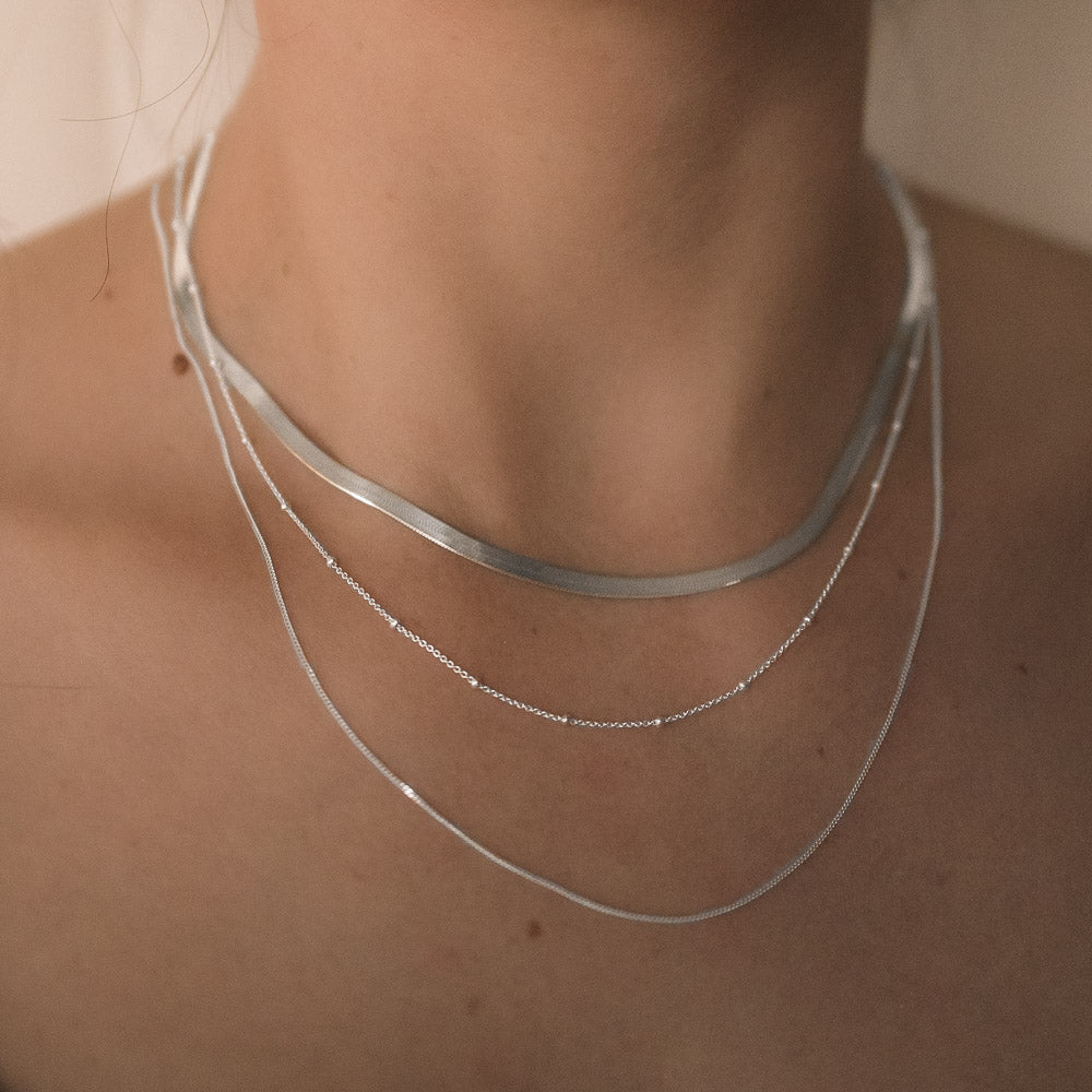 woman wearing three necklace chains herringbone, satellite and curb