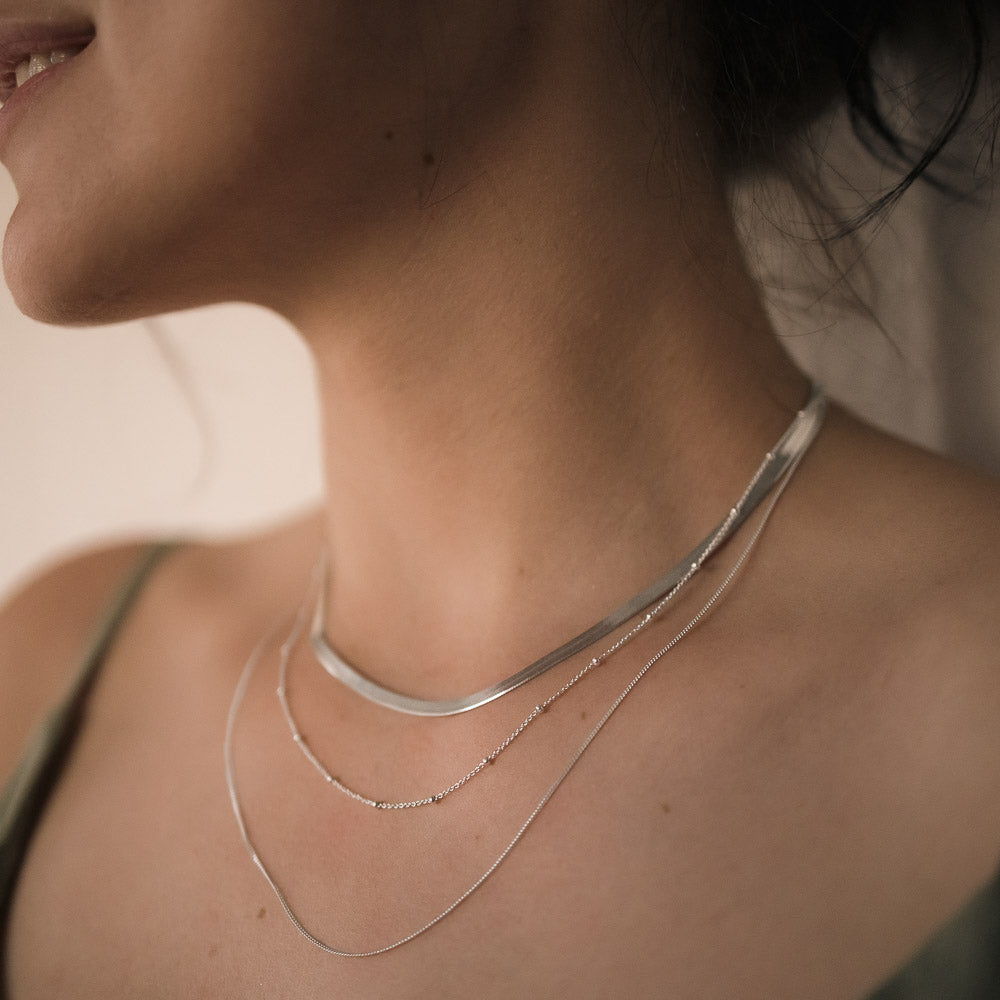 woman wearing three necklace chains herringbone, satellite and curb