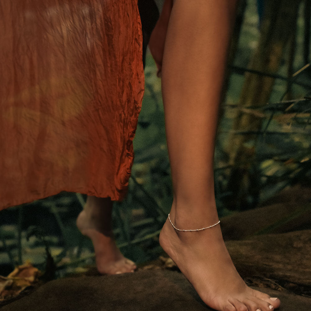 a woman walking through the jungle wearing a silver satellite anklet