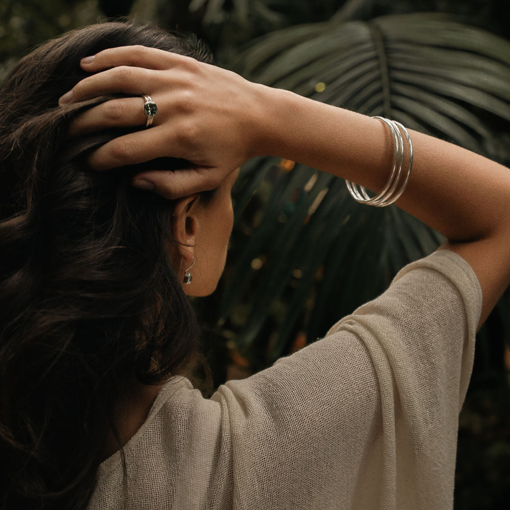 a woman facing the back with her arms up wearing three sterling silver bangles and green amethyst ring