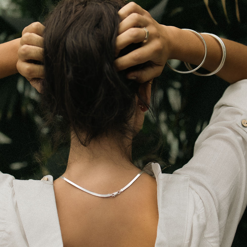 a woman facing her back to the camera wearing a silver herringbone necklace chain