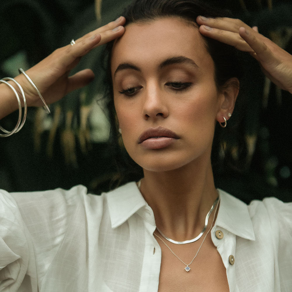 a woman wearing three silver bangles with her hands up to her forehead in the jungle