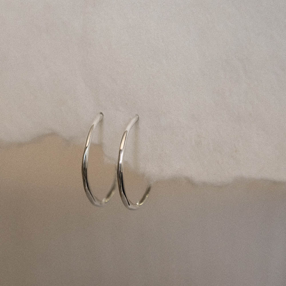 a pair of organic-shaped silver jewellery hoops hanging from handmade paper
