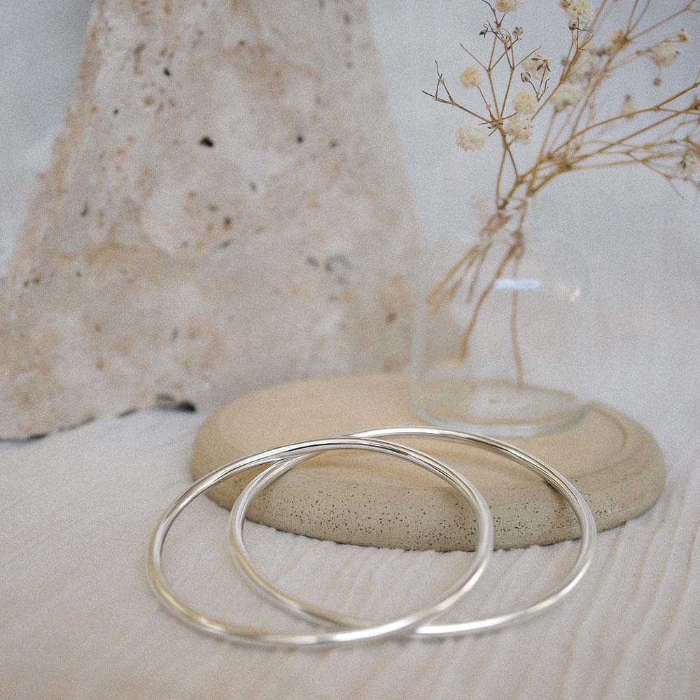 two 3mm wide hollow silver bangles resting up against a ceramic dish with organic flowers in the background