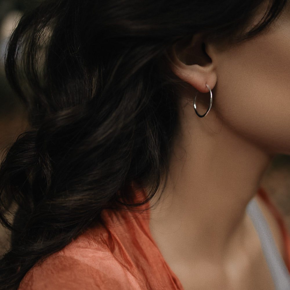 a woman wearing a silver organic-shaped pairs of silver hoops by Inesce Jewellery