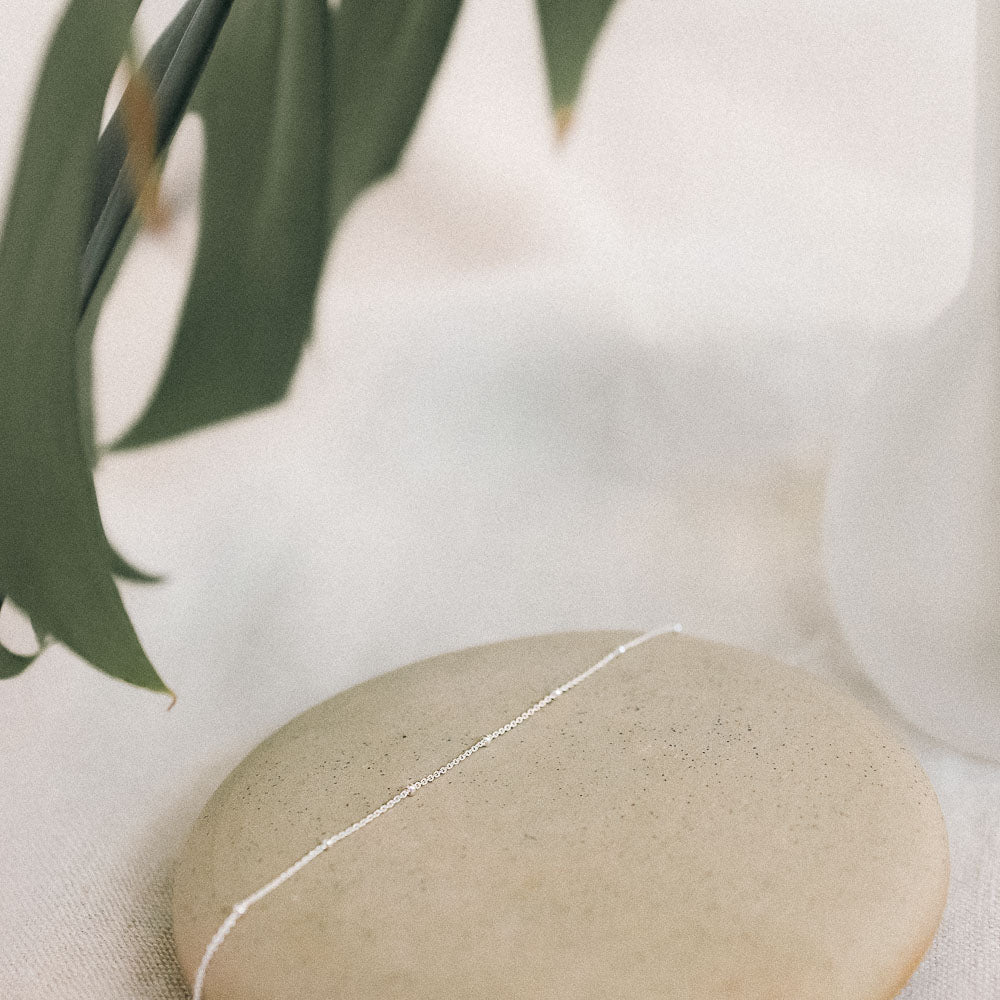 a silver satellite bracelet chain laying on a ceramic dish