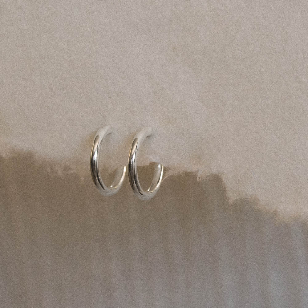 a pair of silver polished hoop earrings hanging on handmade paper by Inesce Jewellery
