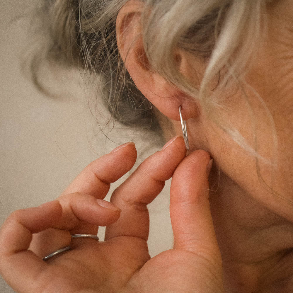 a woman touching a silver organic-shaped pair of silver hoops