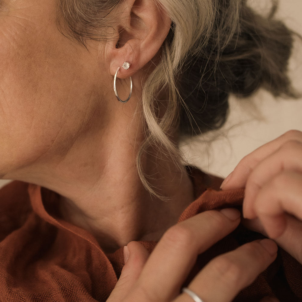 a woman wearing silver organic ripple wave shaped pair of silver hoops by Inesce Jewellery