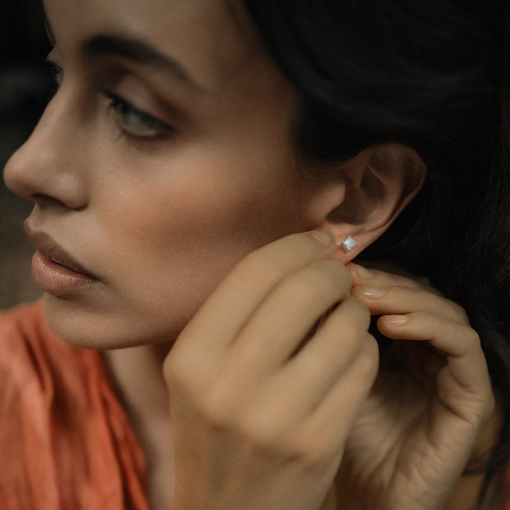 woman putting in square gemstone moonstone earring studs