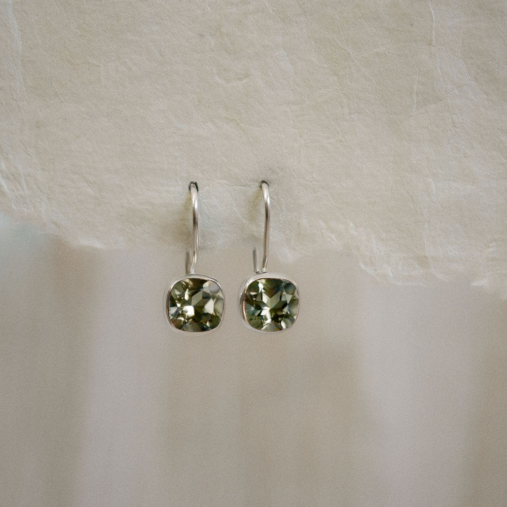 a pair of green amethyst square faceted earrings hanging from handmade paper