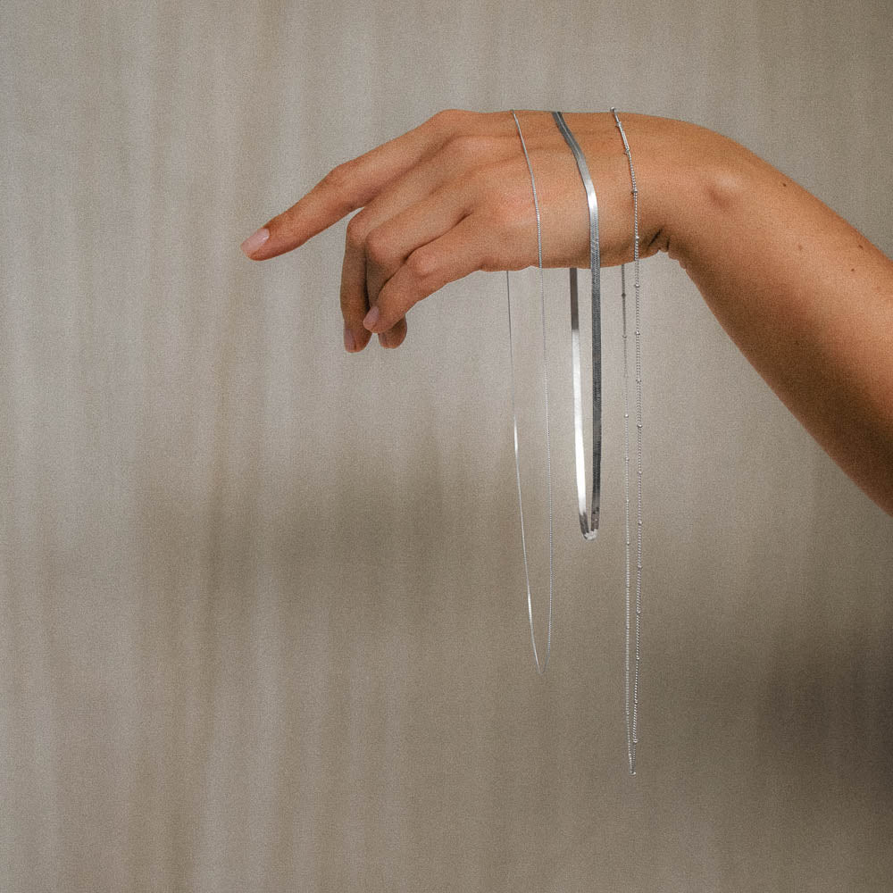 hand holding three hanging necklace chains herringbone, satellite and curb chains