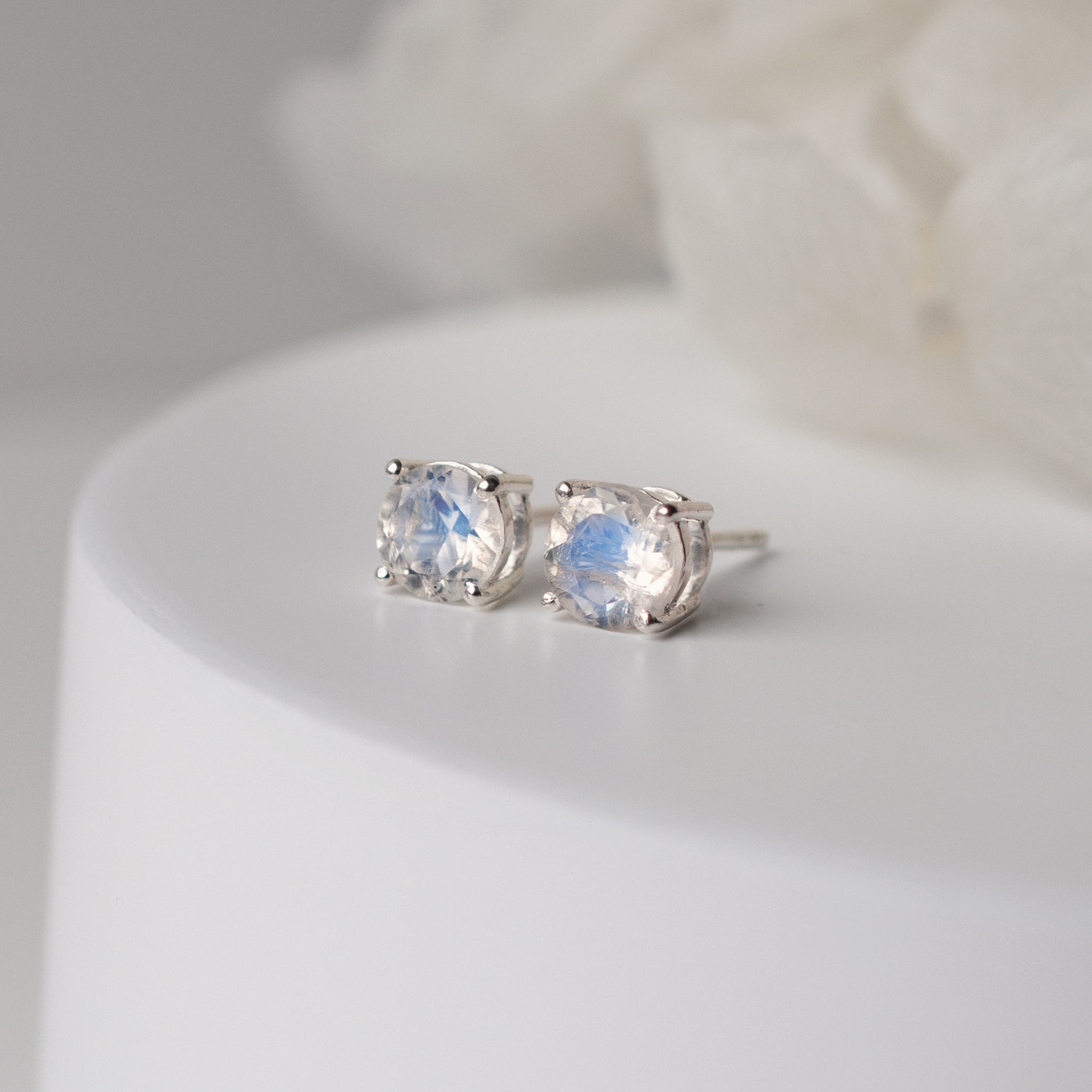 6mm large rainbow moonstone studs resting on a white cylinder with flowers in background