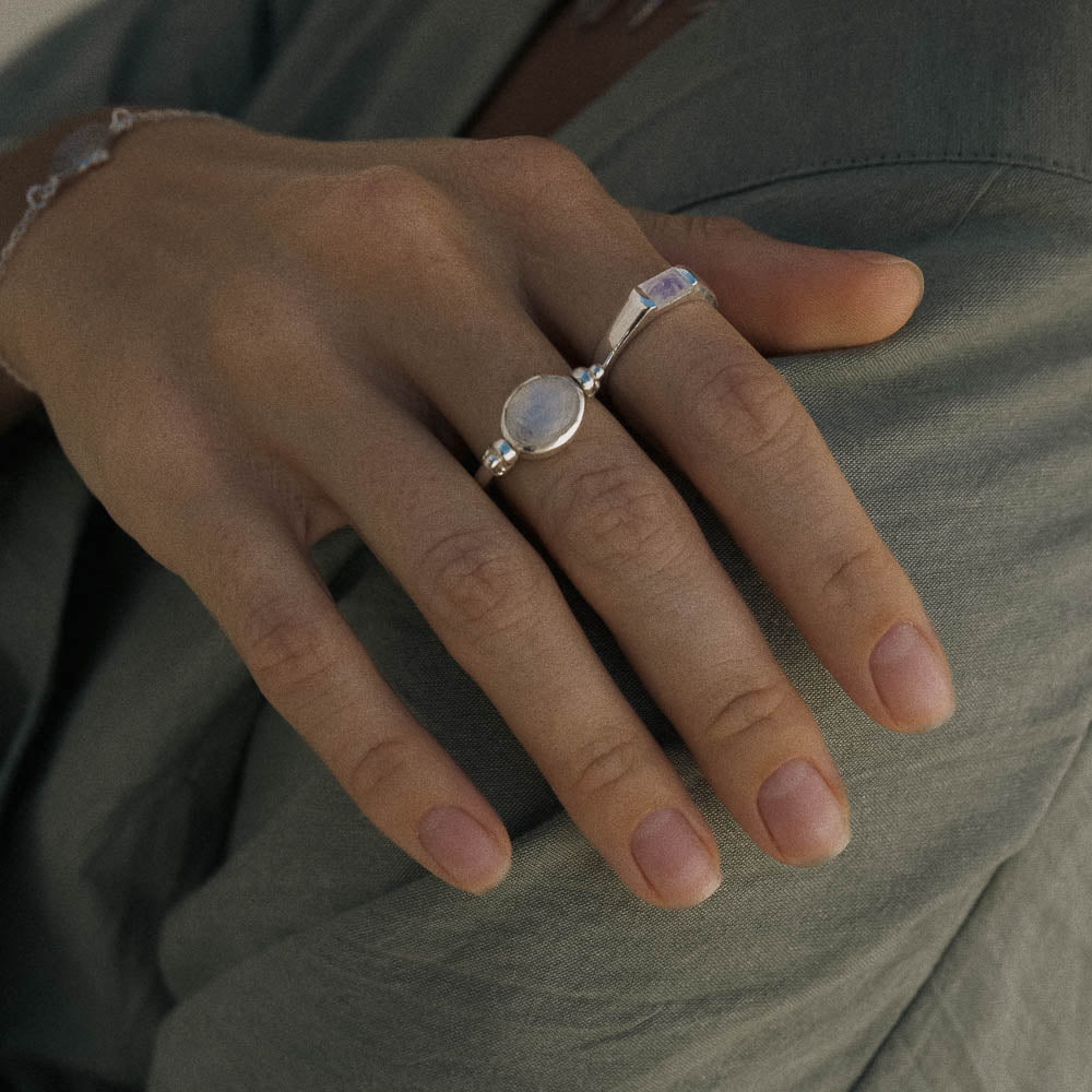 Close-up of a hand wearing a silver ring with a stone on a green fabric background