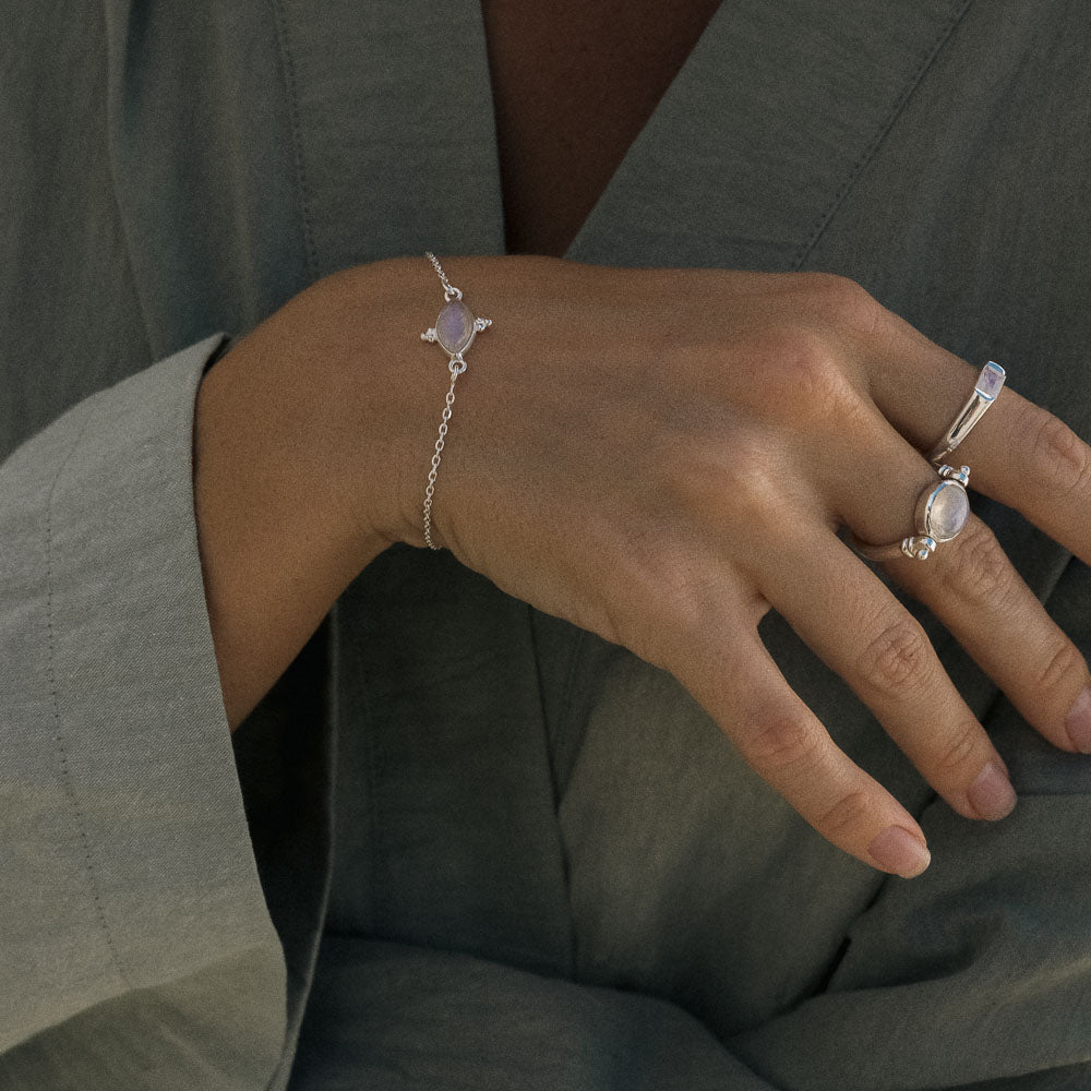 Close-up of a hand wearing a silver bracelet and ring with a green background